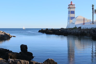 白色和蓝色的灯塔在白天平静的水体旁